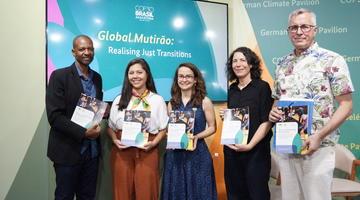 Five speakers holding the INCLUDE guidebook in front of a TV screen